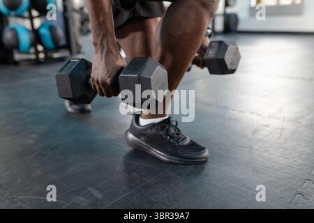 Afroamerikaner, der Hex-Kurzhanteln auf Gummimatten am Medizinballständer im Fitnessstudio hebt Stockfoto