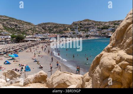 Matala, Kreta, Griechenland - 23. Juni 2025: Touristen genießen das Schwimmen und Sonnenbaden am Matala Strand auf Kreta, umgeben von atemberaubenden Klippen. Stockfoto