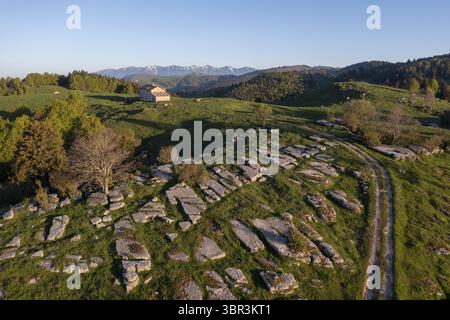 Aus der Vogelperspektive der sonnengeküssten Steinformationen blickt man auf ein einsames Gebäude, das inmitten von sanften grünen Hügeln unter einem riesigen Himmel liegt, Roverè Veronese, Venetien, Italien. Stockfoto