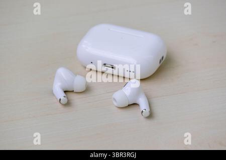 Weiße kabellose Kopfhörer, die neben der Ladetasche auf hölzernem Hintergrund liegen. Moderne Bluetooth-Ohrstöpsel sind einsatzbereit. Stockfoto