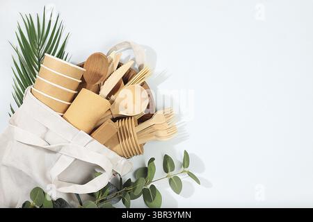 Ein Set umweltfreundlicher Gerichte in einer Öko-Tasche auf einem sonnigen Tisch. Pappbecher, Teller, Kraftpapierservietten, Grillhalme, Holzgabeln, Löffel Stockfoto