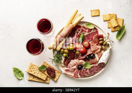Vorspeisen mit verschiedenen Antipasti, Wurstwaren, Snacks und Rotwein auf weißem Hintergrund. Wurst, Schinken, Tapas, Oliven und Cracker für eine Buffetparty. Stockfoto