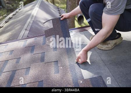 Eine Nahaufnahme der Hände des Meisters auf dem Dach enthält flexible Fliesen Stockfoto
