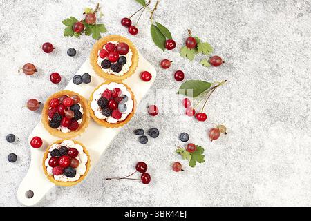 Leckere Tartlets mit frischen Beeren Himbeeren, Kirschen, Stachelbeeren und Heidelbeeren. Cupcakes mit weicher Quark Creme, Sommerdessert. Konzept eines Stockfoto
