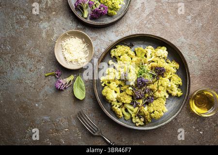 Gebratener grüner und lila Blumenkohl mit Kräutern und Gewürzen auf Teller über grauem Steinhintergrund. Draufsicht Stockfoto