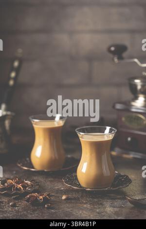 Tee oder Kaffee mit Milch und Gewürzen im Glas Armudu mit Kaffeebohnen und Zucker auf dunklem Hintergrund Stockfoto