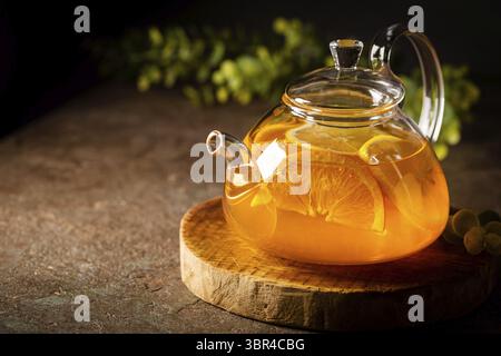 Glas Teekanne mit heißem Zitrustee aus Orangen, Zitronen und Limetten, gesundes Getränk auf dunklem Hintergrund Stockfoto