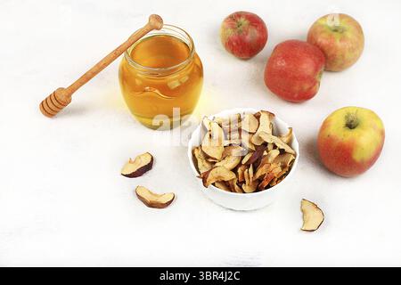 Hausgemachte Apfelchips in einer Tasse mit Äpfeln und Honig auf weißem Hintergrund, im Herbst werden Äpfel im Ofen oder Trockner für Lagerung im Winter gebacken, Feinkost Stockfoto