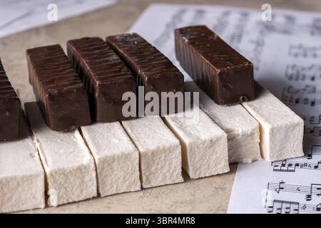 Eine Klaviertastatur aus weißen Marshmallows und Schokolade liegt auf Notenpapier, selektiver Fokus, Nahaufnahme Stockfoto