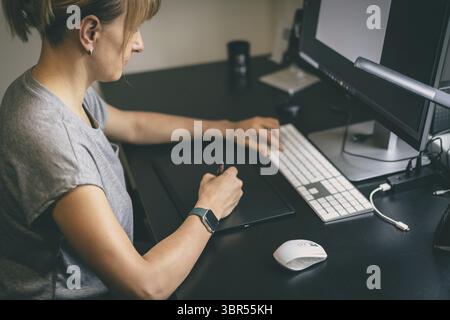 Designerin, Retuscherin, Fotografin oder Künstlerin, die im Home Office etwas auf einem Grafiktablett zeichnet Stockfoto
