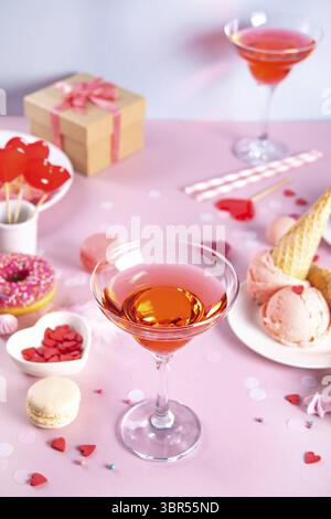 Romantischer süßer Desserttisch mit einem Glas rosa Wein, Waffeln, Donut, Eis, Macaron, lutscher, Süßigkeiten. Valentinstag-Konzept Stockfoto