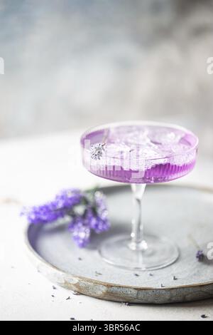 Purple Drink mit Eiswürfeln in einem Glas auf weiß Hintergrund mit Blumen Stockfoto