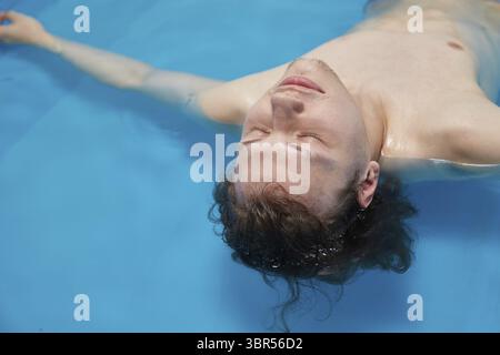 Ein hübscher junger Mann schwimmt im Pool auf seinem Rücken. Entspannung und Spa-Therapie. Kopierbereich Stockfoto