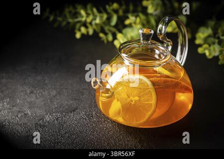 Glas Teekanne mit heißem Zitrustee aus Orangen, Zitronen und Limetten, gesundes Getränk auf dunklem Hintergrund Stockfoto