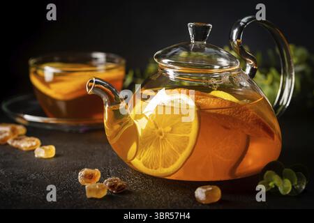 Glas Teekanne mit heißem Zitrustee aus Orangen, Zitronen und Limetten, gesundes Getränk auf dunklem Hintergrund Stockfoto