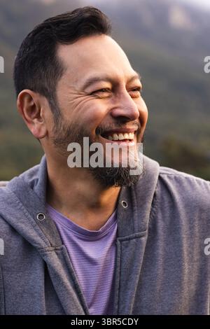 Asiatischer Mann lächelt, während er nach rechts schaut, trägt einen grauen Hoodie und ein violettes Sportshirt in grünen Hügeln Stockfoto