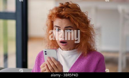 Kaukasische Frau weibliche Nutzerin weibliches Mädchen auf der Heimcouch drinnen schauend Handy Smartphone schlechte Nachrichten Schock staunend negativ verwirrt online Stockfoto