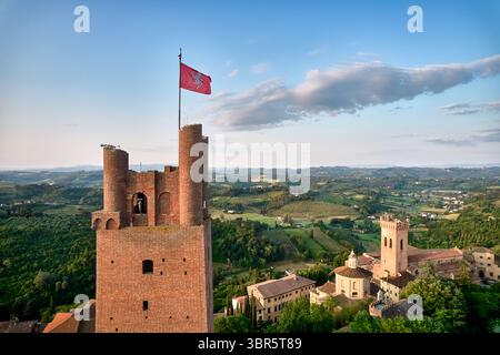 Aus der Vogelperspektive auf einen mittelalterlichen Turm mit einer winkenden Flagge, umgeben von sanften Hügeln mit Terrakottadächern und üppigen grünen Bäumen, San Miniato, Toskana Stockfoto
