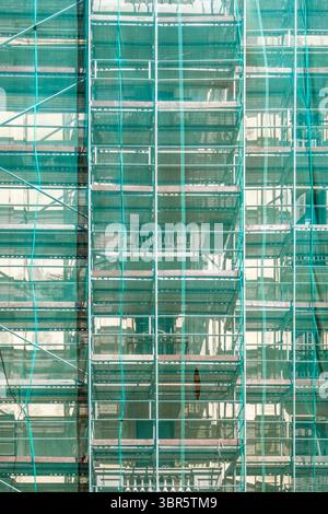 Grünes Baugerüst An Der Gebäudefassade Während Des Renovierungsprojekts Mit Sicherheitsgitter Und Metallrahmen. Städtische Entwicklungsstätte, Architectura Stockfoto