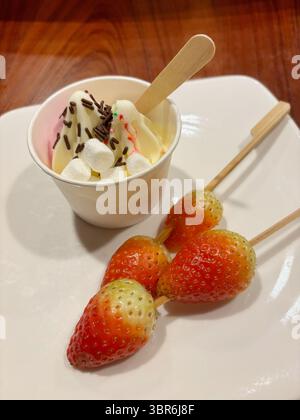 Vanilleweiche servieren mit Schokoladenstreuseln und Marshmallow und Erdbeere auf Spieß, serviert auf einem weißen Teller. Stockfoto