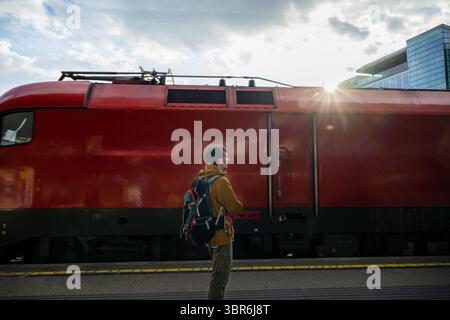 Mann mit Rucksack auf Bahnsteig mit rotem Zug Stockfoto