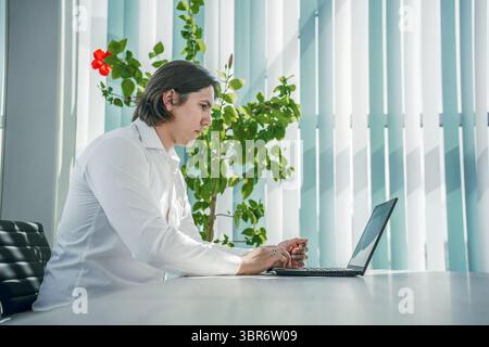 Mann, der am Laptop im Büro arbeitet, nachdenkliche Pose. Moderne Innenausstattung. Stockfoto