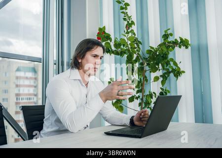 Mann, der am Laptop im Büro arbeitet, nachdenkliche Pose. Moderne Innenausstattung. Stockfoto