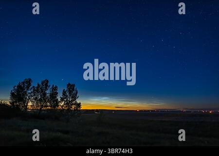 4. Juni 2019: Eine Weitwinkelansicht des Schauplatzes der nächtlichen Wolken am nördlichen Horizont am 4./5. Juni 2019 von zu Hause im Süden Albertas. Dies war um Mitternacht MDT mit Dämmerung, die immer noch den Himmel erhellte, wie es die ganze Nacht zu dieser Jahreszeit aus meinem Breitengrad von 51Â n. .. Cassiopeia ist oben rechts, Capella ist über den Bäumen und Perseus schimmert den nördlichen Horizont in der Mitte. Diese Abbildung zeigt die NLCs im Kontext, um ihre Winkelausdehnung zu zeigen. ..Dies ist ein Einzelbild mit dem 24-mm-Objektiv und der a7III-Kamera von Sony. Die Belichtung betrug 5 Sekunden bei f/2,8 und ISO 800. (Kredit Ima Stockfoto