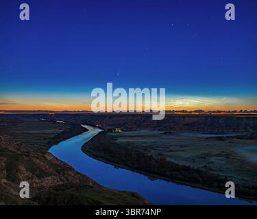 11. Juli 2020, Alberta, Kanada: Komet NEOWISE (C/2020 F3) über dem Red Deer River vom Orkney Aussichtspunkt nördlich von Drumheller, Alberta, am Morgen des 11. Juli 2020. Der Himmel ist hell im Morgengrauen und eine kleine Anzeige von nachleuchtenden Wolken ist rechts am Horizont. Das Sternbild Auriga mit dem hellen Stern Capella ist rechts. Das hier blickt nach Norden zum Bleriot Ferry Terminal. Licht vom abnehmenden Gibbous Mond sorgt für die Beleuchtung und Dämmerung. Etwas Erdnebel liegt im Tal darunter... Dies ist ein vertikales Panorama mit zwei Segmenten und dem 35-mm-Canon Objektiv bei 1:2,8 Stockfoto