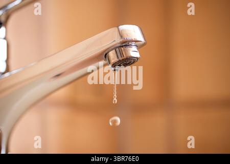 Tropfender Wasserhahn mit Wassertropfen im Badezimmer des Apartments. Makro, Nahaufnahme, geringe Schärfentiefe, keine Personen Stockfoto