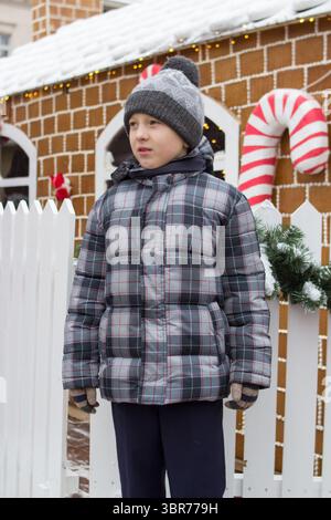 Trauriger Junge, der im Winter auf der Messe in der Nähe des Lebkuchenladens steht Stockfoto