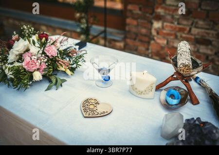 Baum mit Hochzeitsringen. Wunderschön gestalteter spiritueller Tisch mit Kerze, Kristallen und atemberaubendem Blumendekor. Natürliche Hochzeit. Stockfoto
