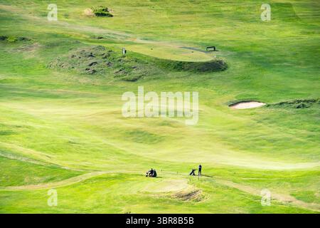 Der Blick auf den lebhaften grünen Golfplatz rollt sanft unter einem weichen Himmel, gespickt mit Golfern und Sandfallen, eine friedliche Szene, Vestmannaeyjabær, Vestmannaeyja Stockfoto