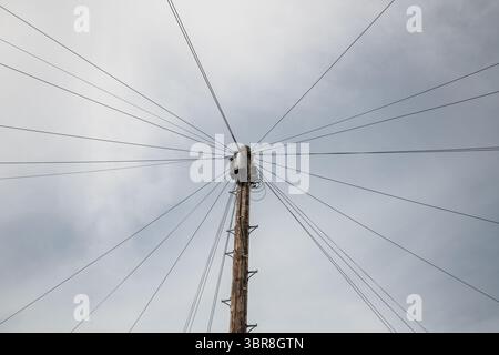 Der Telegrafenmast ist gegen den Himmel geschildert, wobei mehrere Drähte in einem Speichenmuster nach außen ausstrahlen, was eine beeindruckende geometrische Komposition schafft. Stockfoto