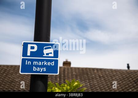 Blaues Parkschild mit einem weißen „P“, eine Fahrzeuggrafik auf einem Bordstein und Text mit der Aufschrift „in markierten Buchten“ – weist nur auf eingeschränktes Parken innerhalb der dafür vorgesehenen AR hin Stockfoto