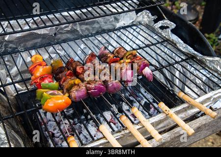 Marinierte Lammkebabs, die auf einem Grill zubereitet werden, mit roten und grünen Paprika und roten Zwiebeln aufgespießt – lebendig, rauchig und voller Geschmack. Stockfoto