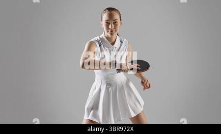 Fokussierte weibliche Athletin, die Tischtennis auf grauem Hintergrund spielt Stockfoto