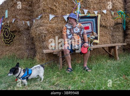 Mann mit zwei Hunden auf einer Holzbank mit Strohballen auf einem Musikfestival Stockfoto