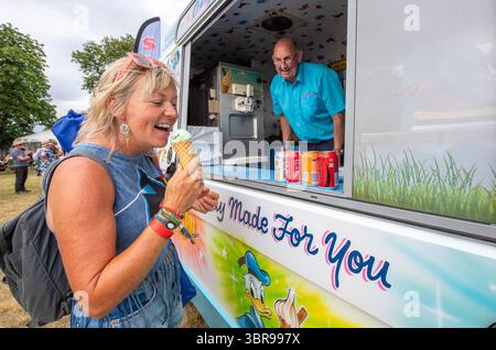 Frau genießt ein Eis aus einem mobilen Eiswagen bei einem Volksmusikfestival an einem heißen, sonnigen Tag. Stockfoto