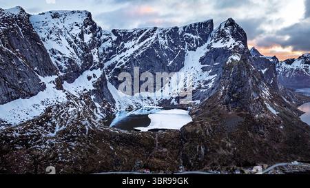 Die majestätischen schneebedeckten Berge durchdringen den Himmel, ihre Gipfel werden vom pastellfarbenen Morgenlicht gemildert und werfen lange Schatten über die stillen Gewässer, reine, Nordland, Norwegen. Stockfoto