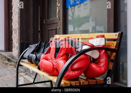 Nahaufnahme von rot-schwarz gefärbten Boxhandschuhen auf einer Holzbank in der Nähe eines Straßeneingangs. Stockfoto