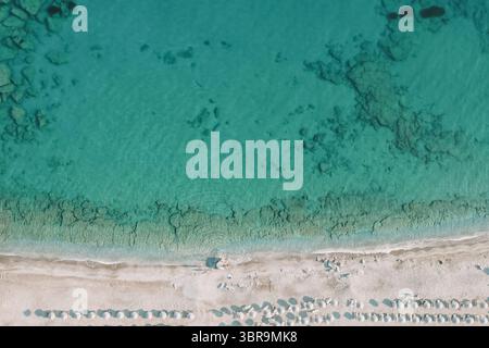 Drohnenfoto der Küstenlandschaft mit kristallklarem Wasser, Unterwasserrelief, weißem Sand und Sonnenschirmen - perfekter Sommerurlaub Stockfoto