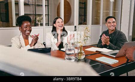Gruppe von verschiedenen Fachleuten, die während eines Meetings in einer modernen Büroumgebung applaudieren und lächeln Stockfoto