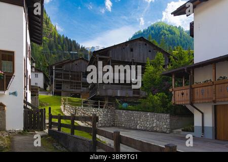 Eine traditionelle Straße in Sottoguda, Dolomitenregion, mit alten Holzscheunen und Alpenhäusern, vor dem Hintergrund üppiger grüner Berge unter einem bl Stockfoto