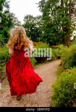 Eine Frau in rotem Kleid läuft einen Weg in einem Garten entlang. Stockfoto
