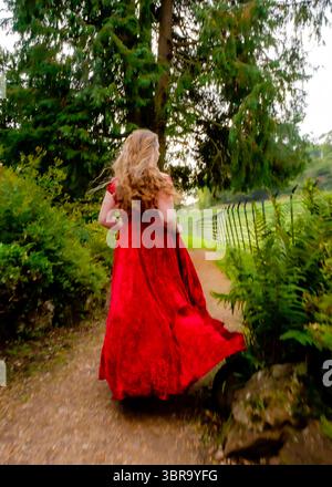 Eine Frau in rotem Kleid läuft einen Weg in einem Park entlang. Stockfoto