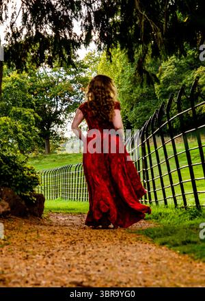 Eine Frau in rotem Kleid geht auf einem Weg in einem Park von der Kamera weg. Stockfoto