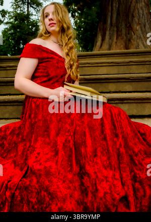 Eine Frau in rotem Kleid sitzt auf der Treppe und hält ein Buch. Stockfoto