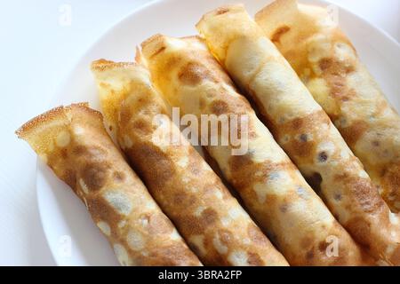 Nahaufnahme von oben von fünf gerollten Crepes mit knusprigen Kanten. Dünne Pfannkuchen gefüllt mit Käse, serviert auf Teller. Rustikale Textur und warme hausgemachte Atmosphäre Stockfoto