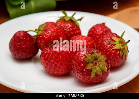Saftige rote Erdbeeren sitzen auf einem weißen Teller und laden im Sommer zum Genuss ein. Stockfoto